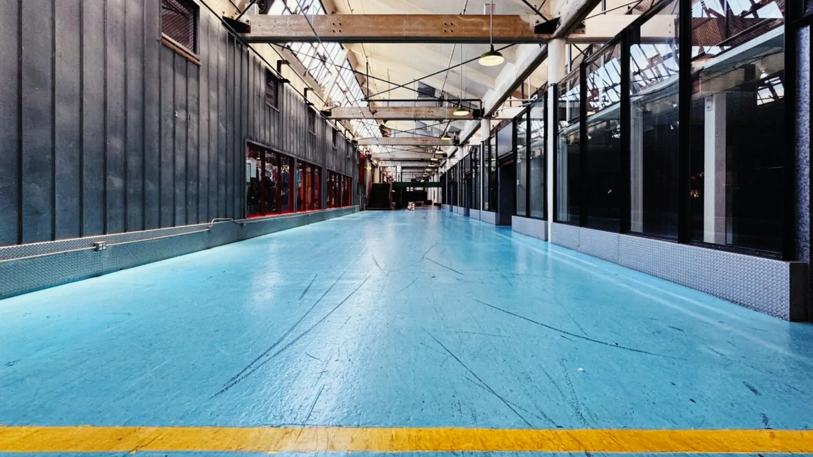 Pasillo amplio con suelo de resina azul y una franja amarilla de señalización